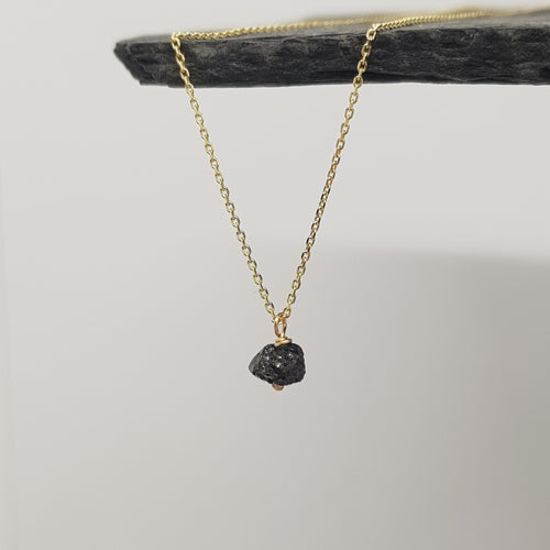 raw black diamond on 9ct yellow gold chain necklace, handmade in the UK. displayed hanging from a black slate